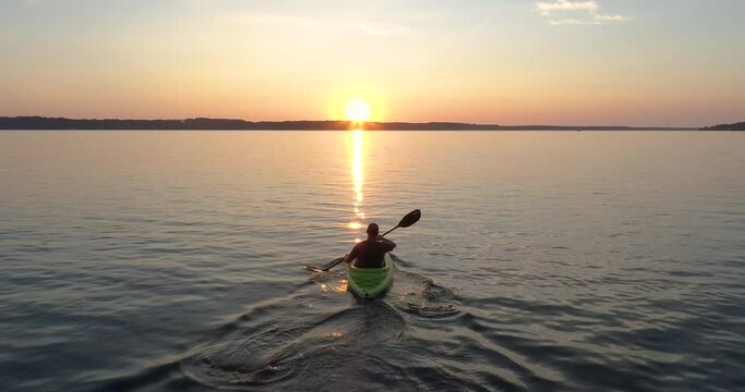 Person kayaking on lake paddling into the sunset.  