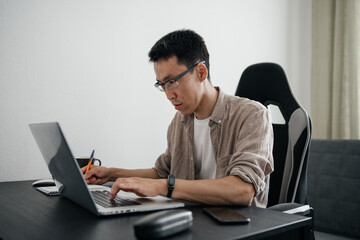 Middle aged asian man working at home with laptop.