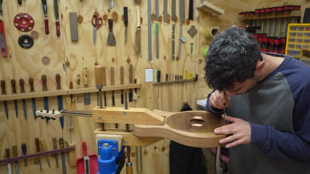Luthier refining the slots by hand filing on cover plate attached to body of newly build electric resonator guitar.