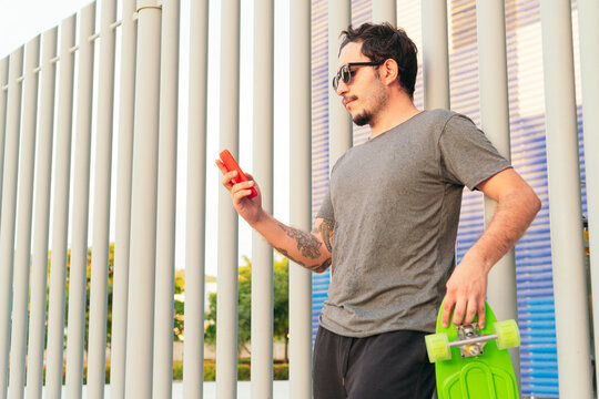 man with sunglasses and skateboard checking his cell phone in the park on a sunny day.