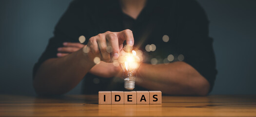 hand touching on light bulb on wood block with Word Ideas, new idea concept with innovation and...