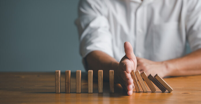 Risk and Strategy in Business, Hand stopping wooden block domino business crisis effect or risk protection concept, prevention and development to stability...