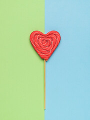 Red heart-shaped candy on a green and blue background. Minimal concept of sweet life and love.