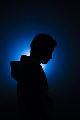 Cleanly define silhouette of man looking down wearing hood blue background