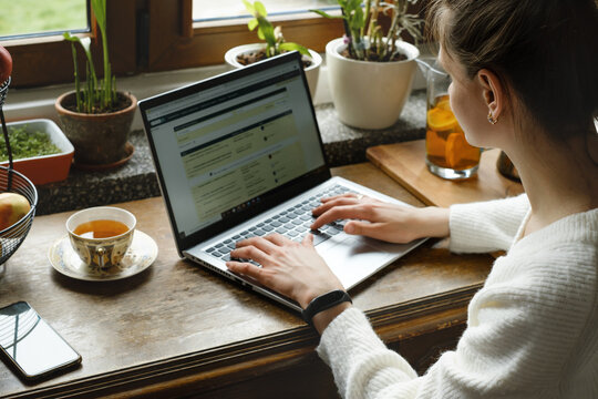 Young freelancer working on laptop at home. Woman using computer on the kitchen for work. Distant job, working remotely in cozy vintage house. Searching education on-line. Adult studding by window