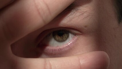 Person with closed eyes covered with fingers in dark shadow. Suddenly big brown eye opens slowly at bright shining sunlight extreme closeup
