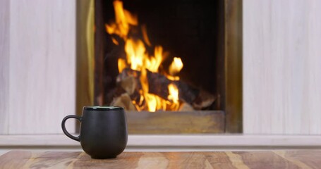 Fire burns in fireplace, firewood, hand puts mug on floor . Atmosphere of warmth, comfort on cool winter evening. Country rest near warm hearth. Rest on by fire, relaxation, manifestation of care.
