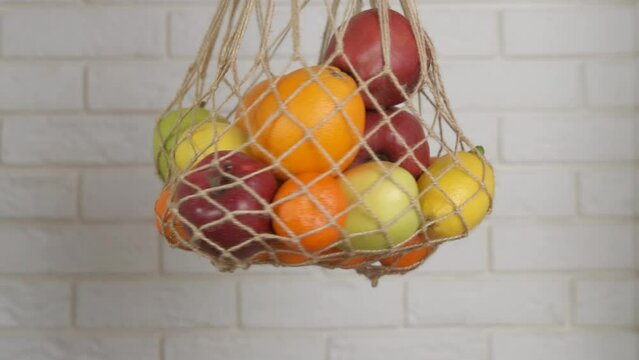 Shopper for fruits. A woman hold an string eco mash with fruits on the table.