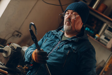 Blacksmith forges and checking tempered metal horseshoe in jar with water at forge.