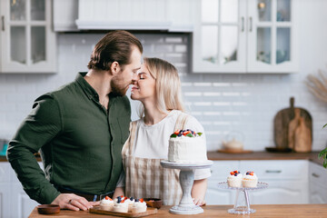 Pastry chef confectioner young caucasian woman with husband boyfriend man try taste of cake on kitchen table. Cakes cupcakes and sweet dessert