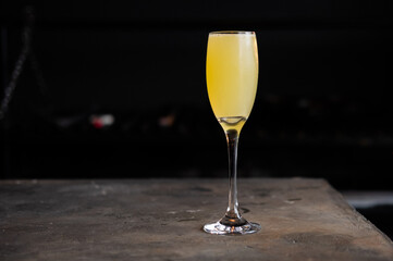 refreshing yellow cocktail served in a glass with ice inside a bar with a black background