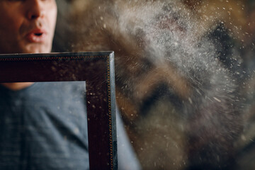 Framing Workshop. Master blows off dust baguette handmade picture frame at studio.