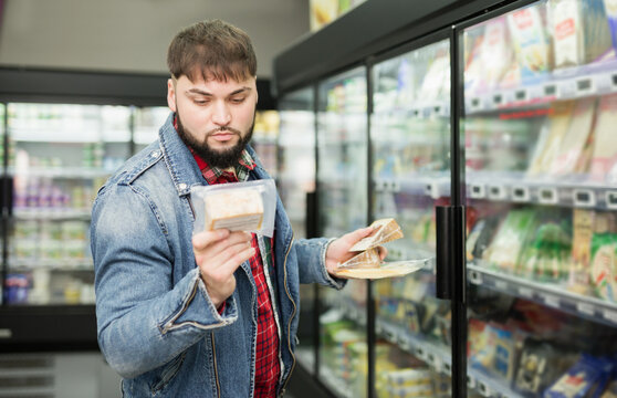 Interested young man shopping in grocery store, looking for hard cheese ..