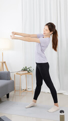 Beautiful Asian woman in sportswear is warming up or doing light exercises in the house with dumbbells and a protein shake or bottle of water and using a laptop at home, Healthy exercise.