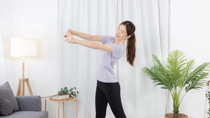 Fototapeta na wymiar Beautiful Asian woman in sportswear is warming up or doing light exercises in the house with dumbbells and a protein shake or bottle of water and using a laptop at home, Healthy exercise.