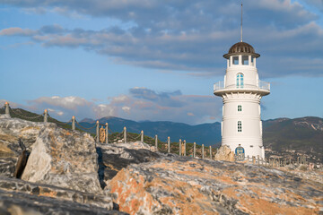 Fototapeta na wymiar White port lighthouse on the background of mountains and sky and clouds.