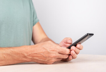 Man hands closeup holding phone with thumb at screen for clicking, swiping, texting message. Male sitting at desk and using smartphone