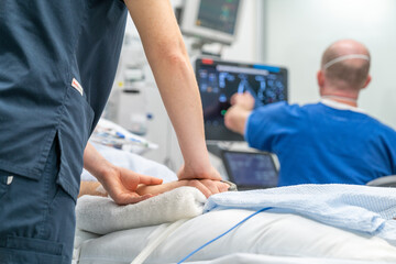Intensive care nurse checking a patient's pulse with doctor in the background looking at a monitor