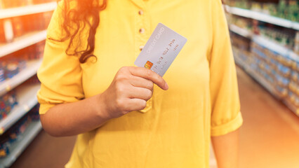  hand holding credit card blur supermarket store background. Woman at the supermarket she is paying credit card shopping concept. Credit card shopping in supermarket hand holding credit card payment.