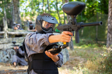 Excited paintball player in protective uniform aiming and shooting with guns