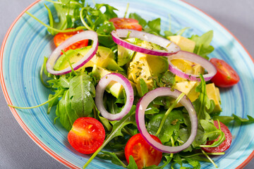 Healthy arugula salad with avocado, cherry tomatoes and onion served on colored ceramic plate