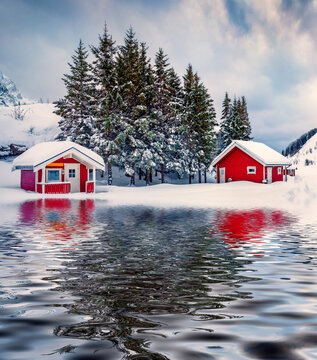 Traditional Norwegian red wooden houses reflected in the calm waters of Kongsjordpollen fjord, Vestvagoy, Norway, Europe. Impressive winter scene of Lofoten islands. Life over polar circle.