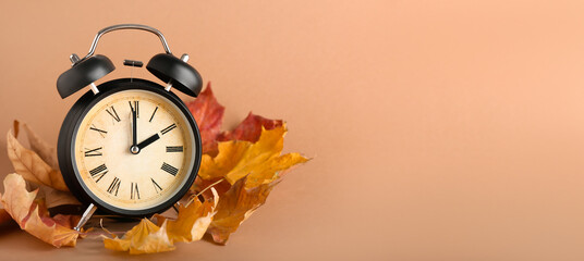 Alarm clock and autumn leaves on color background with space for text