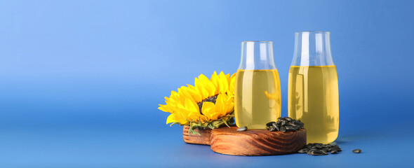 Bottles of oil and sunflowers on blue background with space for text