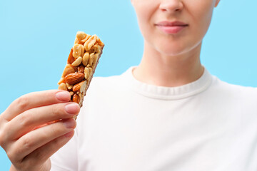 Young woman eating protein bar on a blue background close-up.