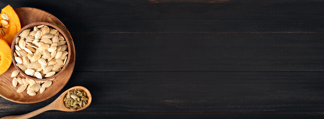Bowl and spoon with natural pumpkin seeds on black wooden background with space for text, top view