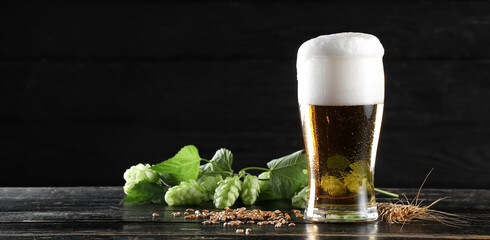 Glass of fresh beer on wooden table against dark background