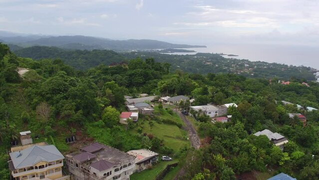 Aerial view and reveal of Port Antonio in Jamaica over the hilltop area of Drapers with the camera pulling away from homes built on the hillside