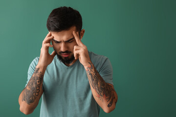 Young bearded man with headache on green background
