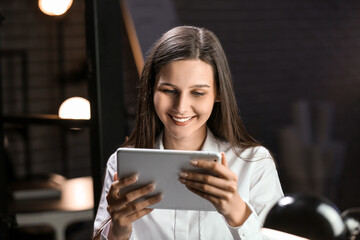 Smiling businesswoman working with tablet computer in office at night