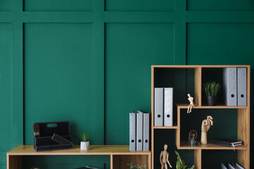 Wooden shelving unit with folders and decor near green wall