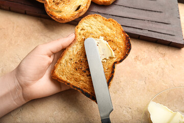 Woman spreading butter onto toast on color background, closeup