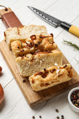 Board with tasty Italian focaccia on light wooden background, closeup