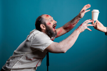 Halloween evil monster wanting coffee cup in studio over blue background, going after desired drink...