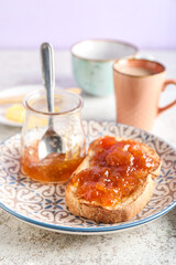 Plate with tasty toast, jar of apricot jam and spoon on grunge background, closeup