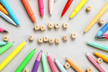 Text LEARN SPANISH with cubes and pens on grey background