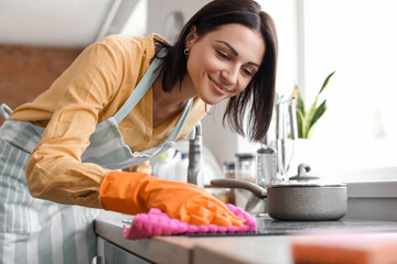 Young woman cleaning electric stove with rag in kitchen