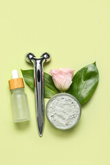 Facial massage tool with cosmetic dropper bottle, clay, rose and leaves on green background