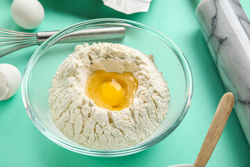 Glass bowl of flour with egg on color background, closeup