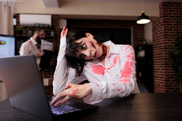 Walking dead corpse looking at laptop, sitting at office desk and being dangerous. Brain eating woman monster with bloody gory wounds being dramatic and eerie with mouth open, violence.