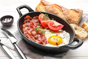 Frying pan with tasty fried egg, bacon and tomatoes on light wooden background, closeup