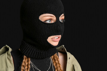 Young woman in balaclava looking aside on black background