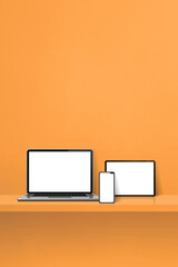 Laptop, mobile phone and digital tablet pc on orange wall shelf. Vertical background