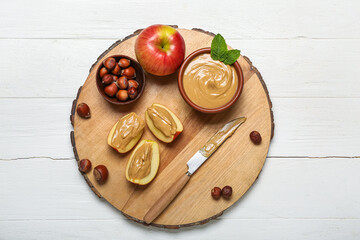 Board of tasty apple wedges with nut butter and hazelnuts on light wooden background