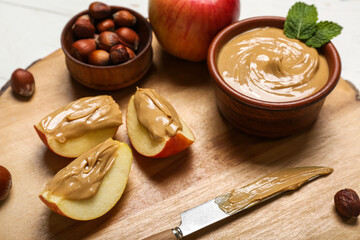 Wooden board of tasty apple wedges with nut butter and hazelnuts, closeup