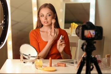 Young beauty blogger applying makeup foundation with brush while recording video at home